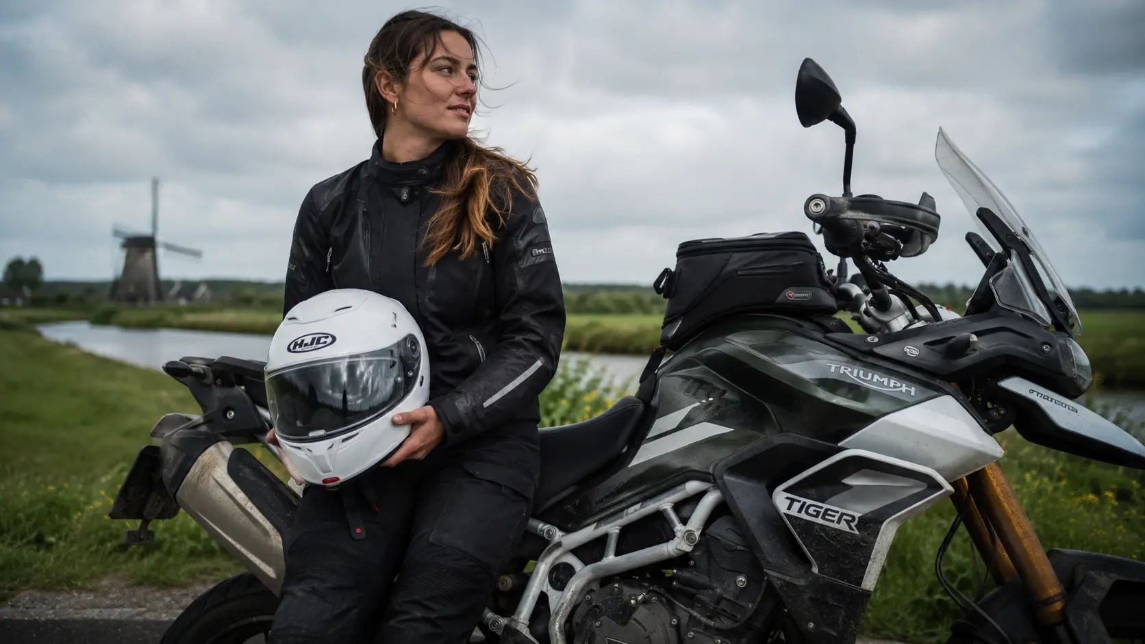 Een vrouwelijke motorrijder neemt pauze langs een polderweg met haar witte HJC RPHA 71 motorhelm voor dames, passend bij een nuchtere praktijktest.