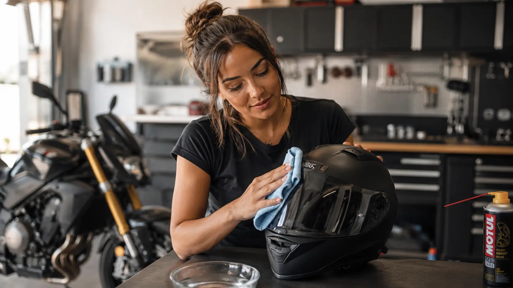 Een motorrijdster maakt de buitenschaal van haar matzwarte motorhelm schoon in een lichte garage met een zachte microvezeldoek.
