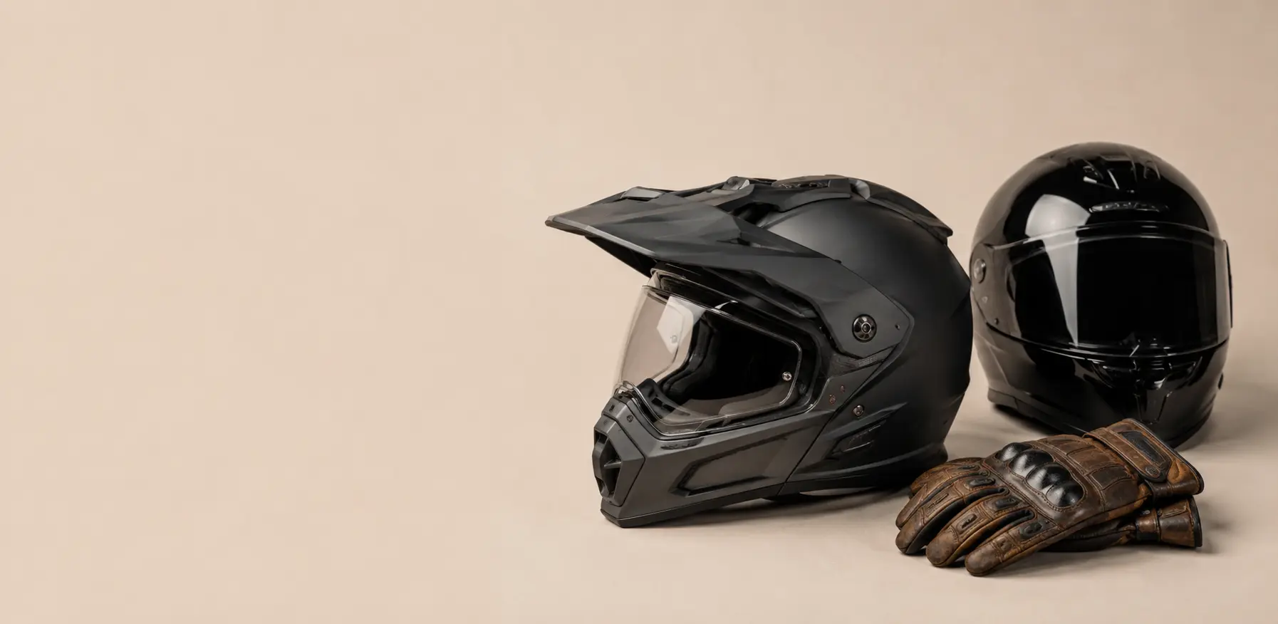 Een minimalistische weergave van verschillende types motoruitrusting, waaronder een adventure helm, race helm en klassieke lederen handschoenen op een lichte achtergrond.