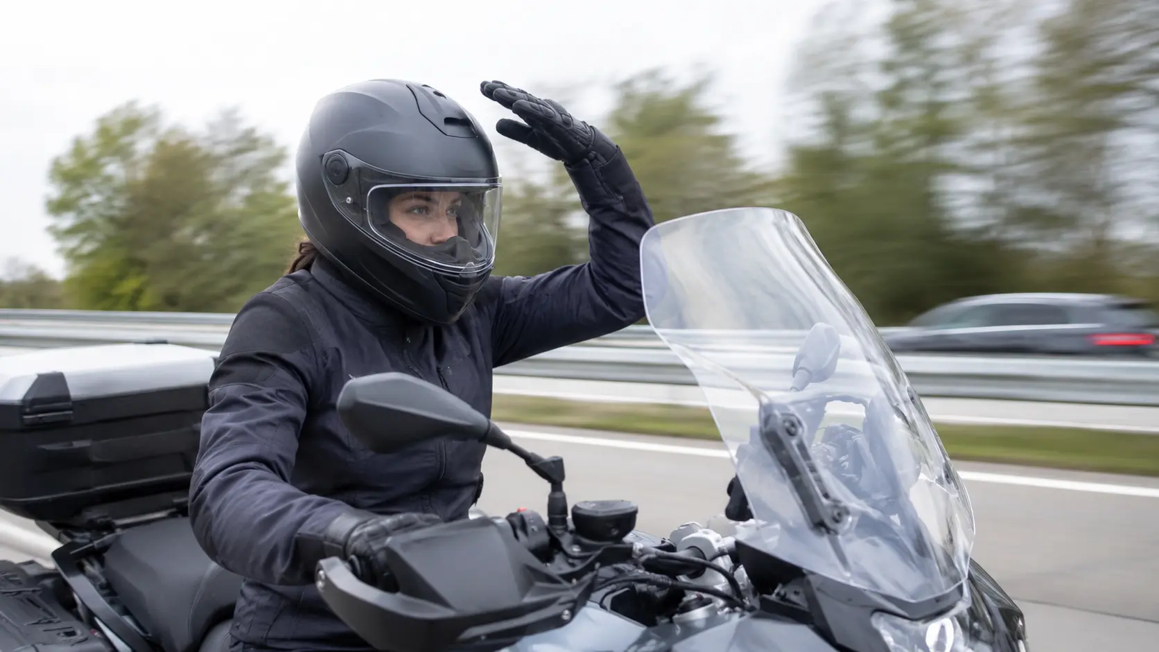 Een motorrijdster houdt tijdens het rijden op de snelweg haar hand net boven haar helm om de turbulente luchtstroom van het windscherm te voelen.