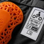 Een close-up van een oranje D3O protector en het officiële CE Level 2 en Klasse AA veiligheidslabel aan de binnenkant van een motorjas.